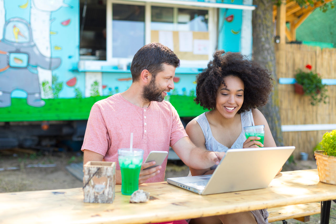 Couple enjoying nature vacations, drinking green cocktails and using laptop.