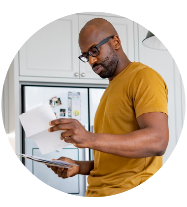 A man in a yellow shirt standing in his kitchen looking through his mail