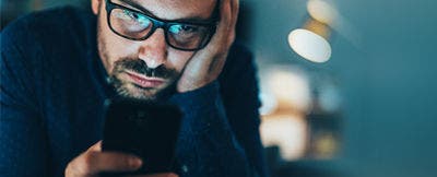 Man with glasses looking at a smartphone.