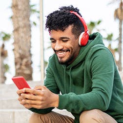 smiling man wearing a hoodie and headphones using a smartphone