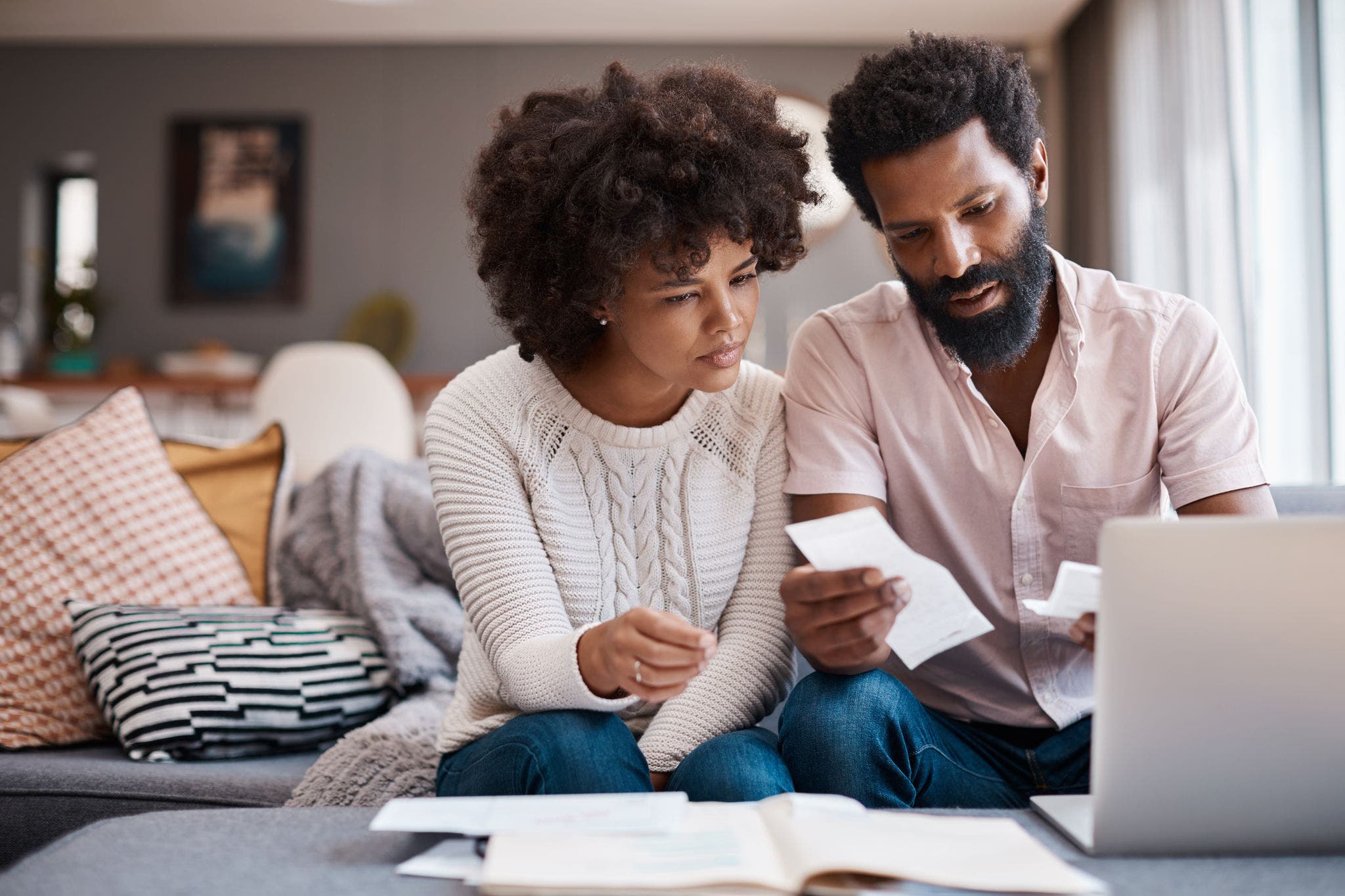 Shot of a couple looking at paperwork while using a laptop in their living room