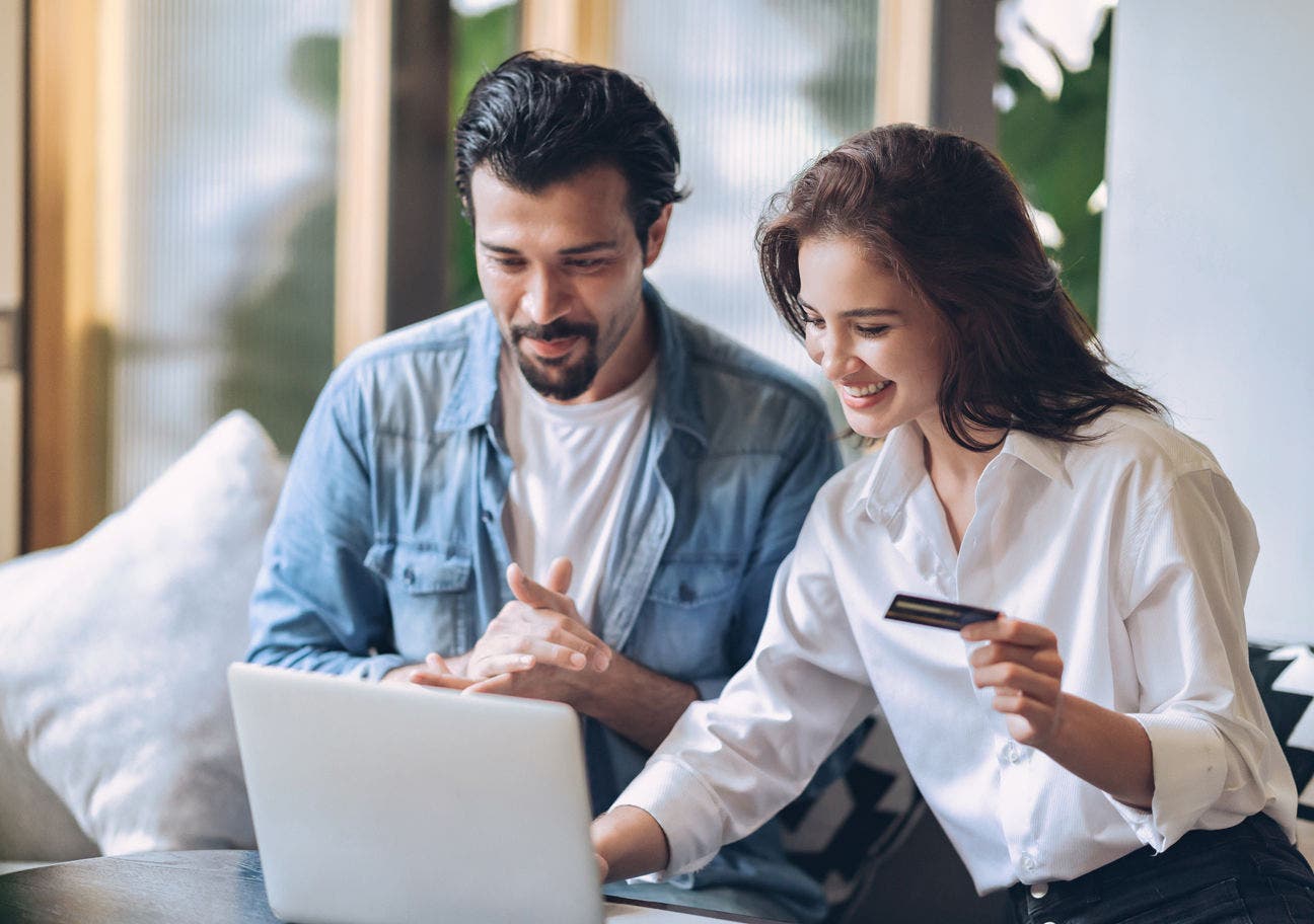 man and woman sitting on a couch using a laptop while the woman holds a credit card