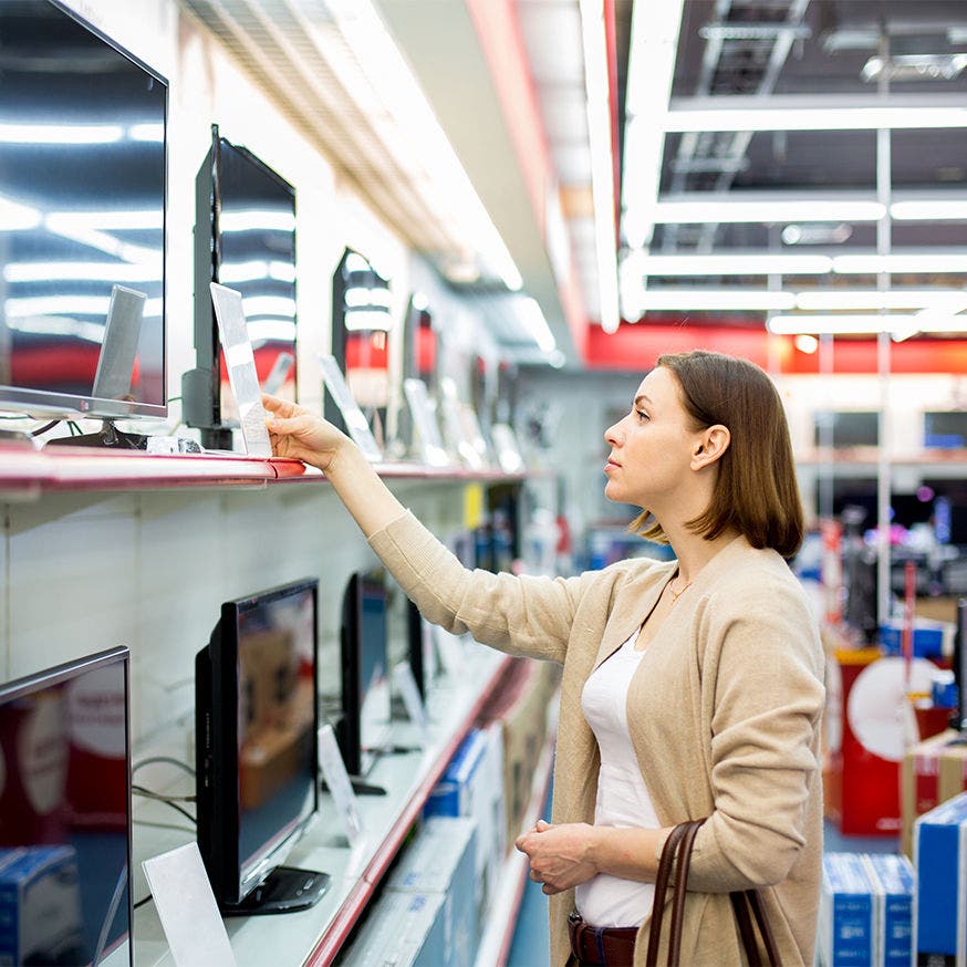 Woman in a store looking at price tags on tvs for sale
