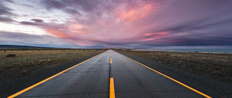 Image of a sunset over a paved two lane highway.