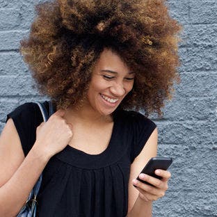smiling woman standing in front of a brick wall looking at a smartphone