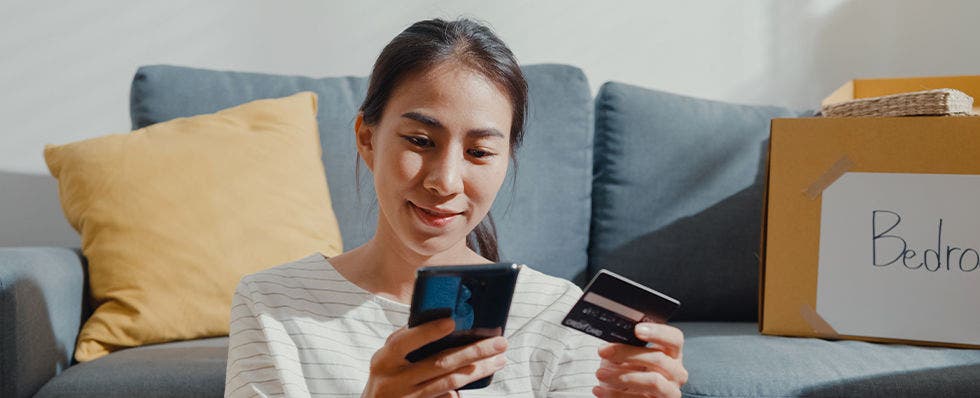 Woman sitting on the floor in front of her couch looking at phone and credit card
