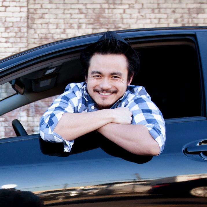 man leaning out of car driver's seat smiling at viewer