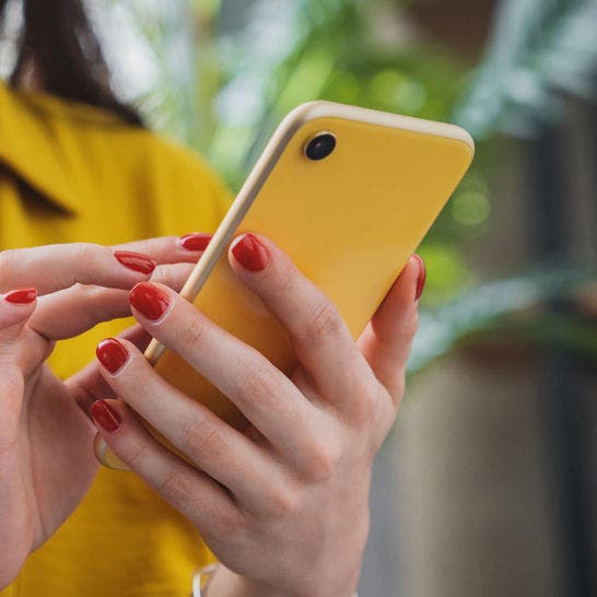 hand with red manicure holding a yellow phone