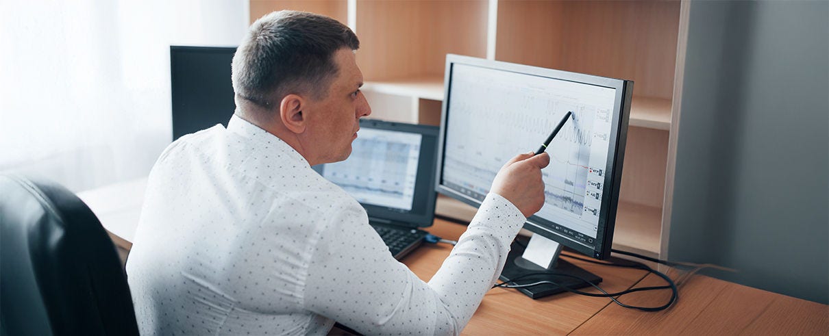 man in office pointing at monitor with pen