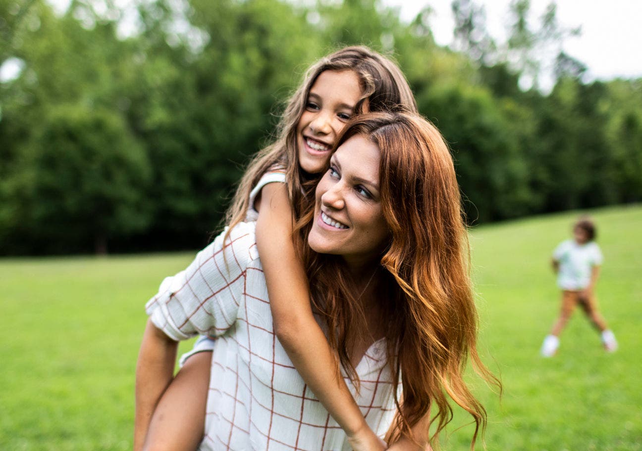 woman giving girl a piggyback ride in a playfield