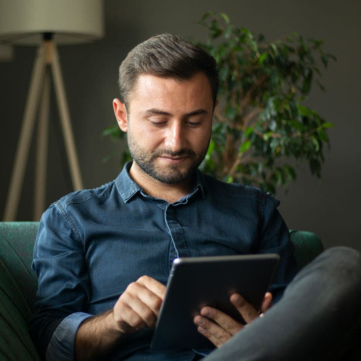 man sitting on couch using tablet