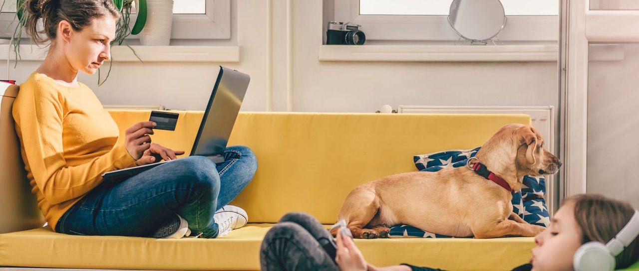 Woman wearing yellow sweater sitting on yellow sofa at home and shopping online with credit card.