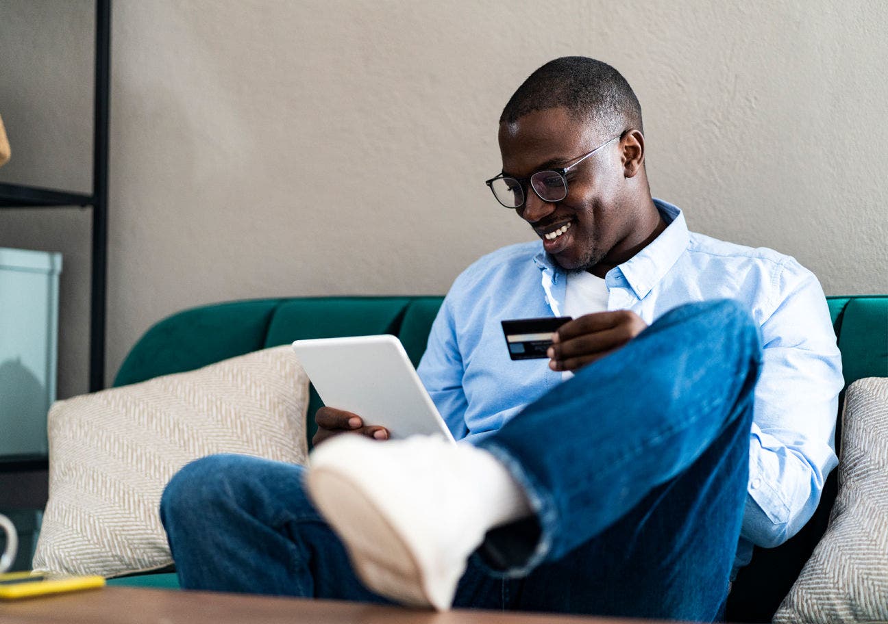 man sitting on couch holding tablet and credit card