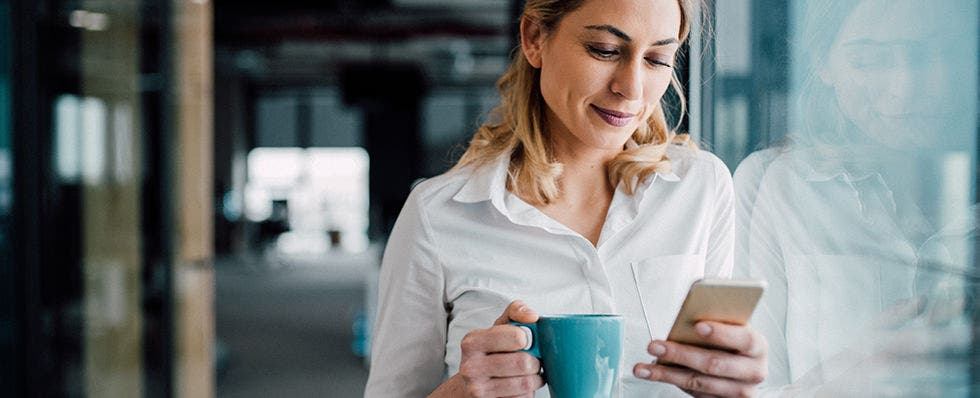 Woman with coffeecup viewing mobile phone
