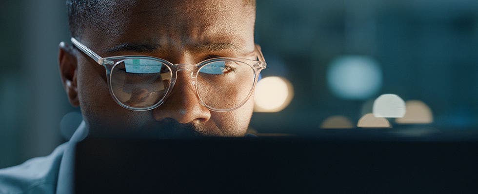 Photo of a man wearing glasses who is looking at a computer screen.