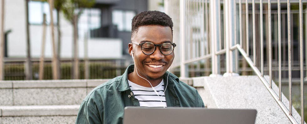 Millennial male listens to headphones and smiles at laptop