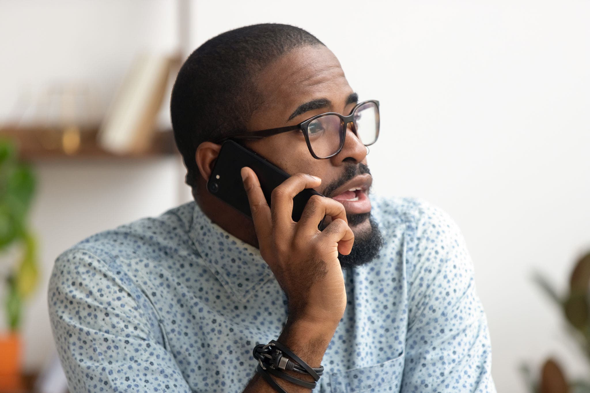 Close up african-american employee talking phone at workplace in office. Black serious businessman speaking on mobile, negotiating, consulting client, solving problem, discussing project with coworker