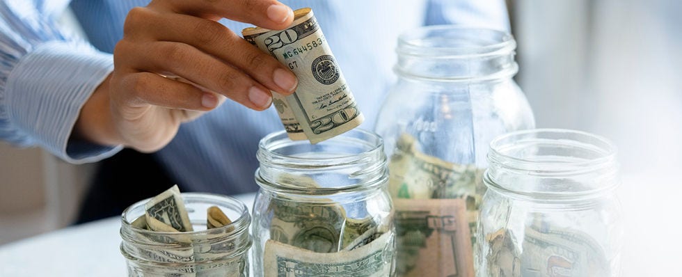 Person putting $20 bill into a jar with other bills. 