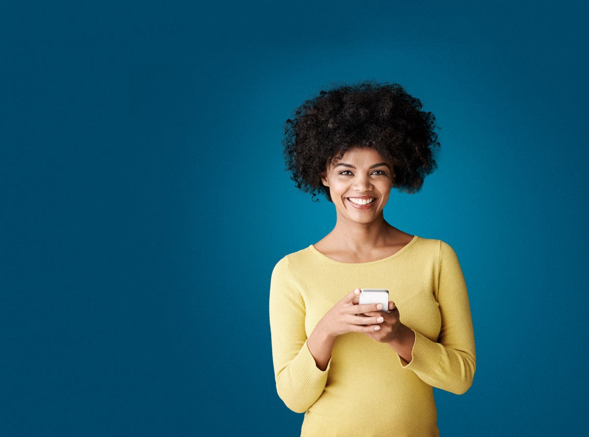 woman in yellow blouse smiling holding a mobile phone