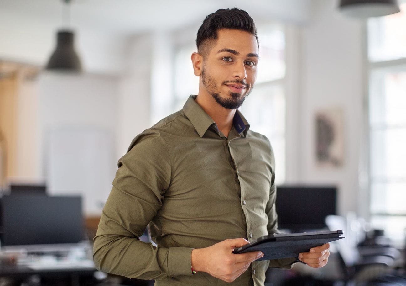 man in an office holding a tablet looking at the viewer