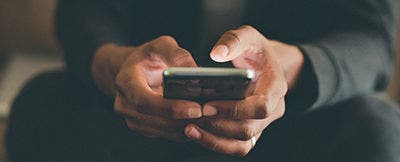 Man holding his cell phone while typing on a laptop