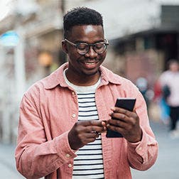 Man wearing a light pink jacket over a striped t shirt looking at his phone