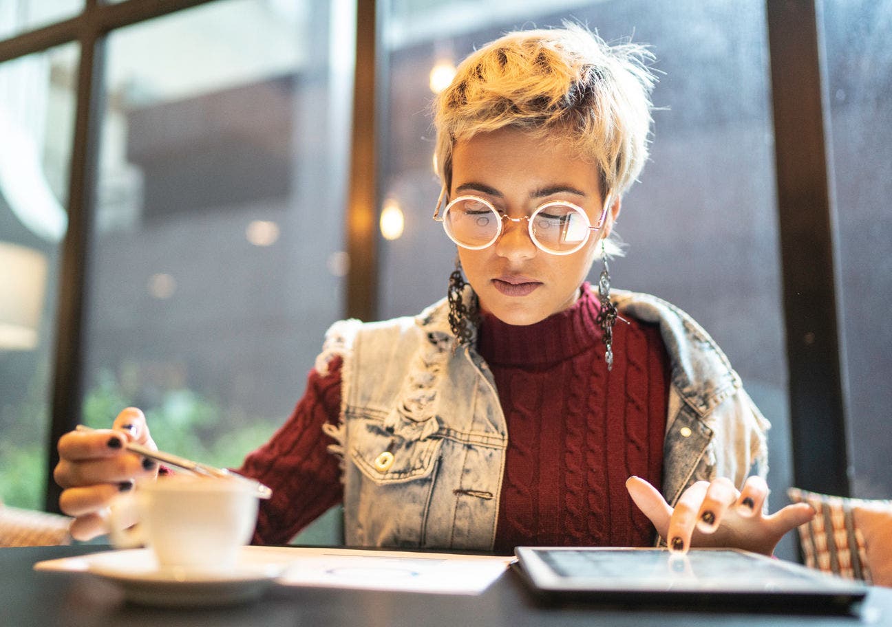 young woman looking at a document and using a tablet at a coffee shop