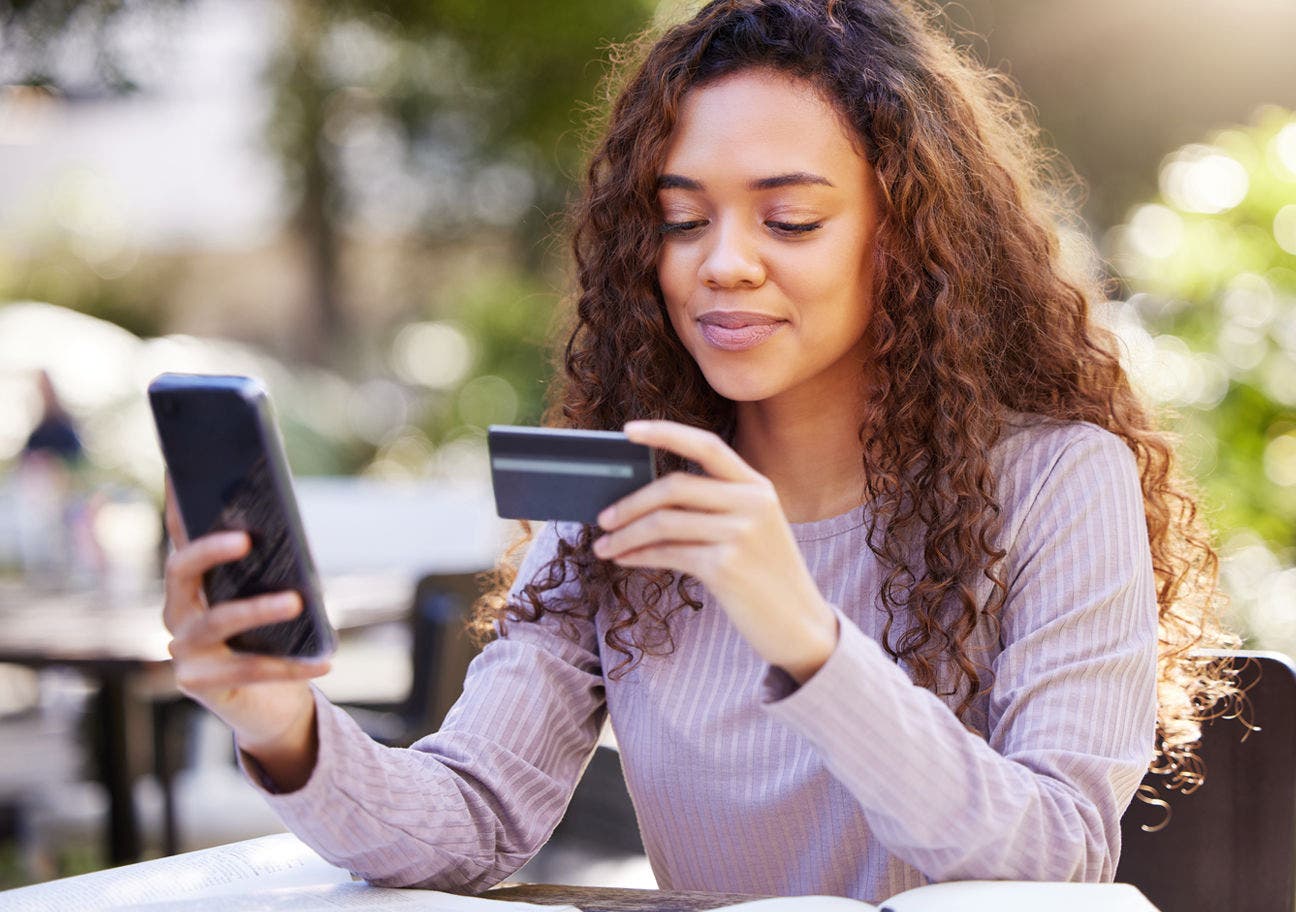 woman sitting in an outdoor cafe holding a credit card and a smartphone