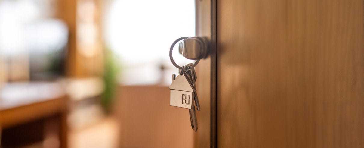 open door with key hanging in lock on house keychain