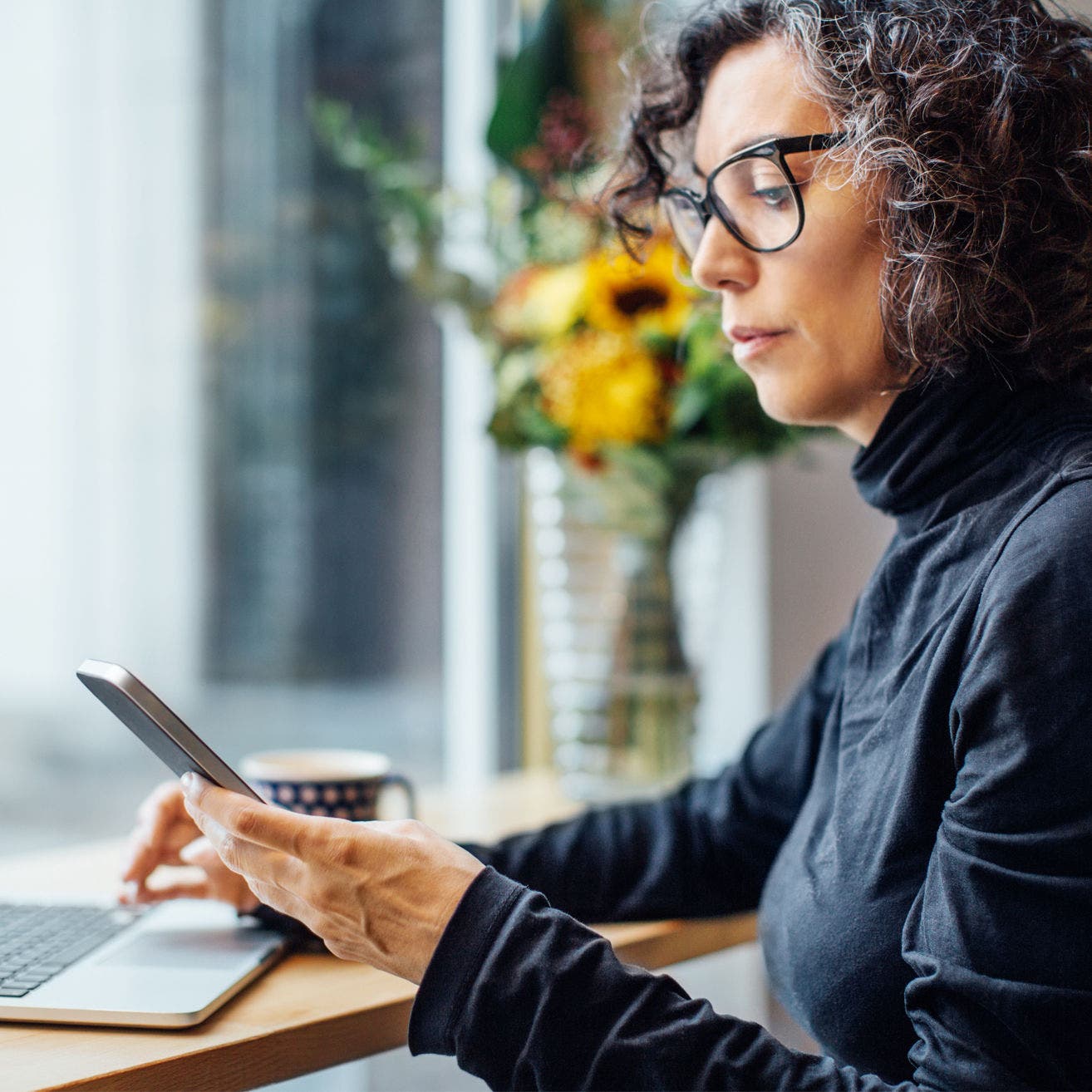 woman looking at mobile phone next to laptop