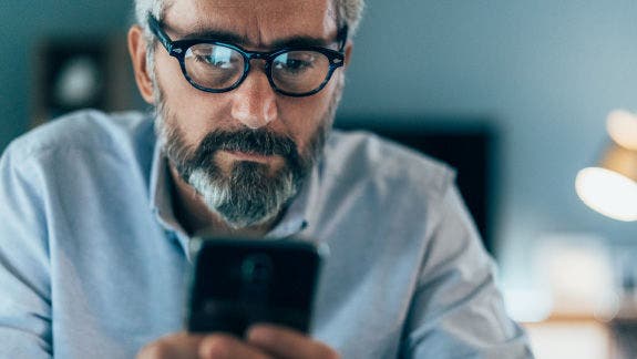 Photo of a man with eyeglasses and a beard looking at a smartphone.