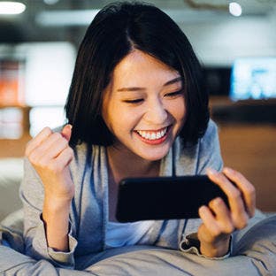 woman sitting on bed using a smartphone and happily punching the air