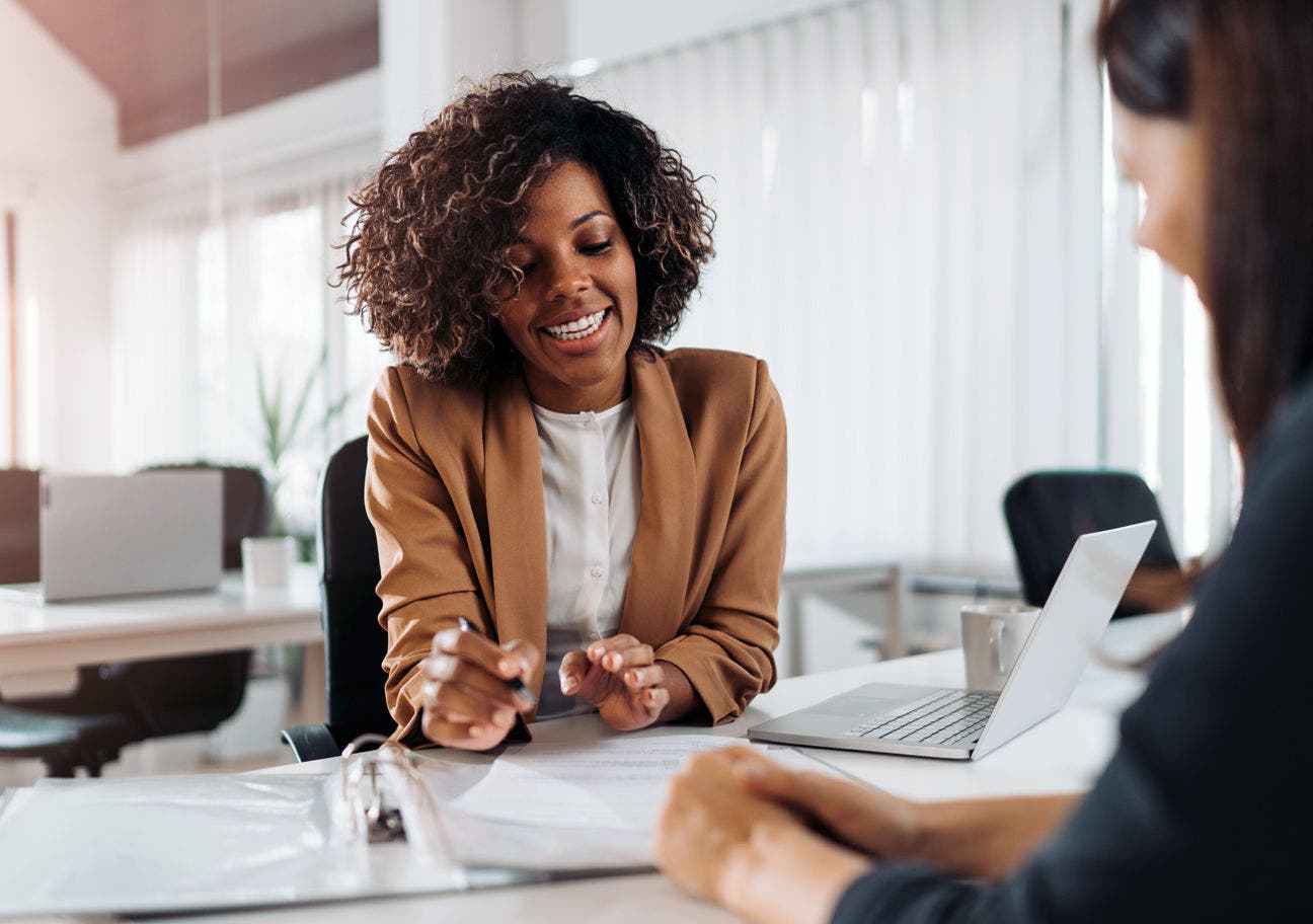 woman sitting at a desk explaining something to another woman