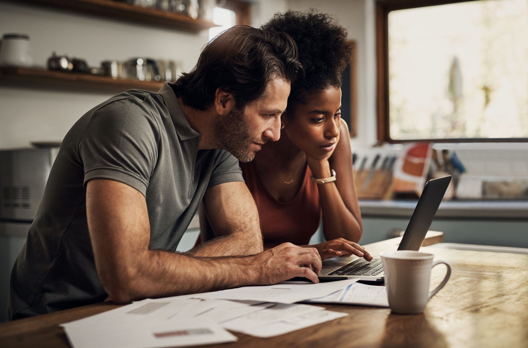 Couple with a laptop doing finance paper work, paying debt insurance loans or online ebanking together at home. Two serious people planning and looking at financial document, bills rate for mortgage.