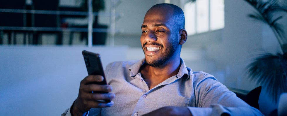 man looking at mobile phone screen illuminating on his smiling face