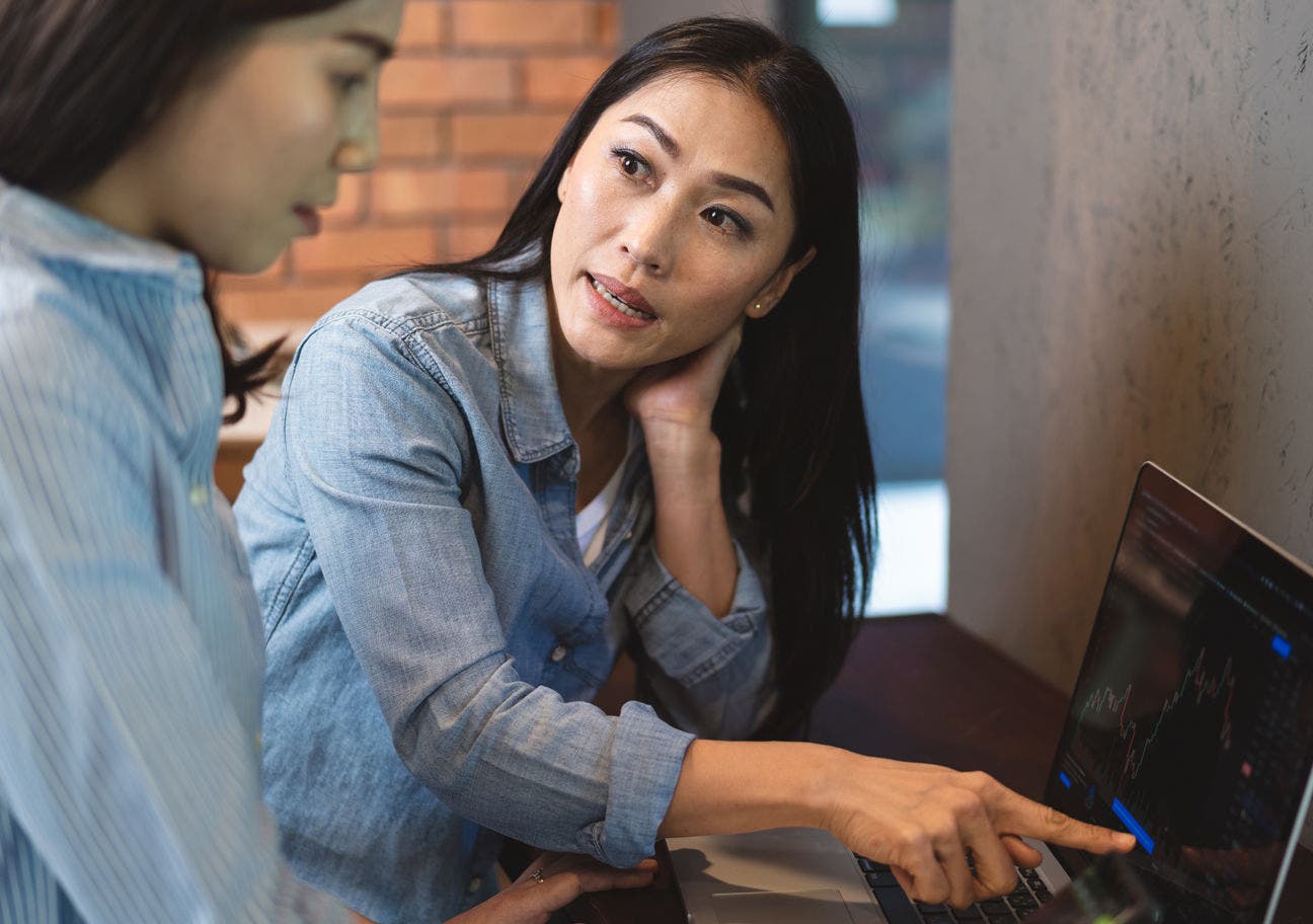 woman pointing at a laptop screen while talking to another woman