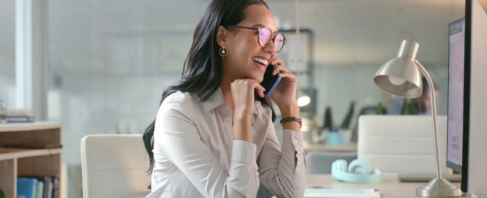 Photo of a woman wearing glasses and dressed professionally who is talking on a mobile device.
