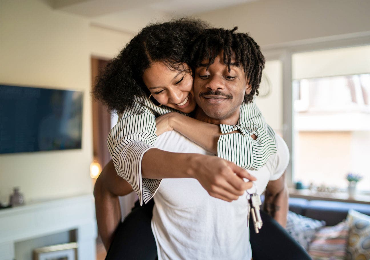 woman hugging man from behind with house keys in her hand