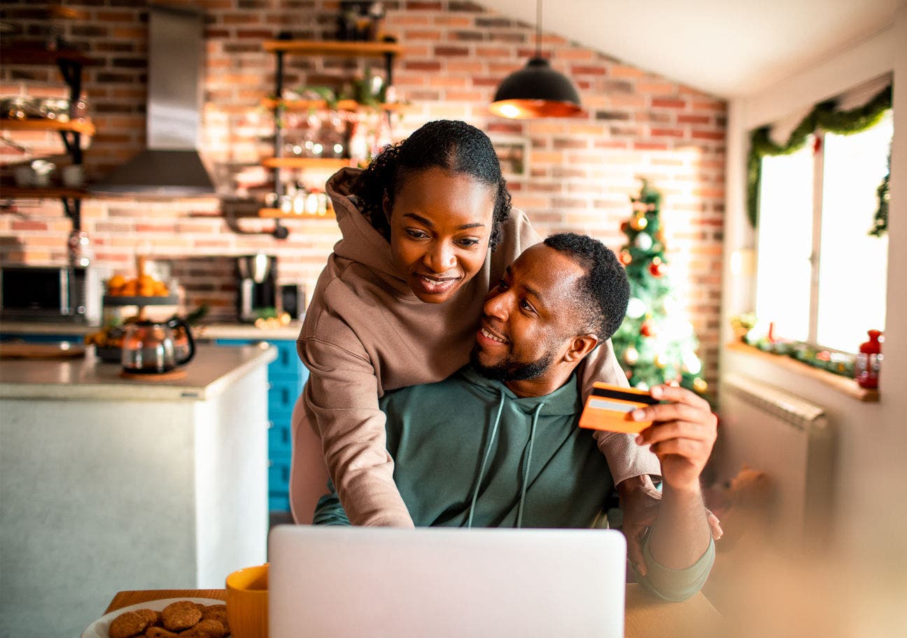 woman leaning over a man's shoulder to use a laptop while he holds a credit card