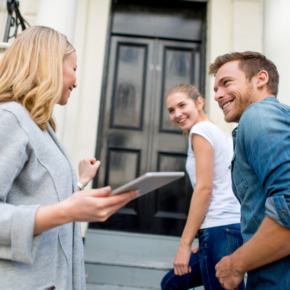 smiling couple talking to woman with tablet in hand