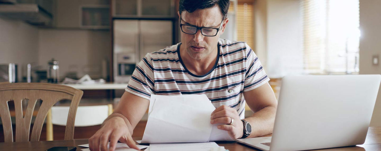 Person reviewing credit report documents at table with laptop and bills