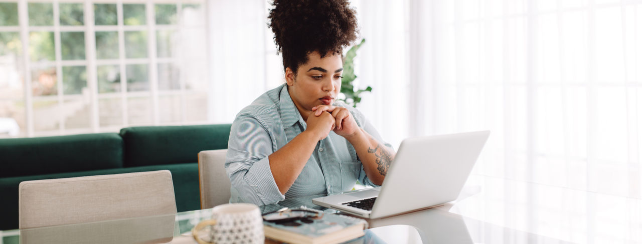 Female sitting on table and looking at laptop. Woman sitting at taking in living room and working on laptop computer at home.