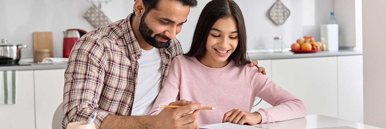 Father holding a pencil teaching his child in the kitchen. 