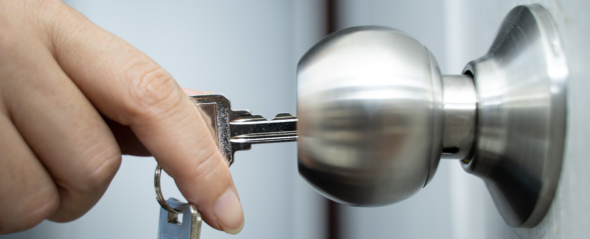 hand holding key inserted into silver doorknob