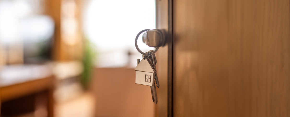 open door with key hanging in lock on house keychain