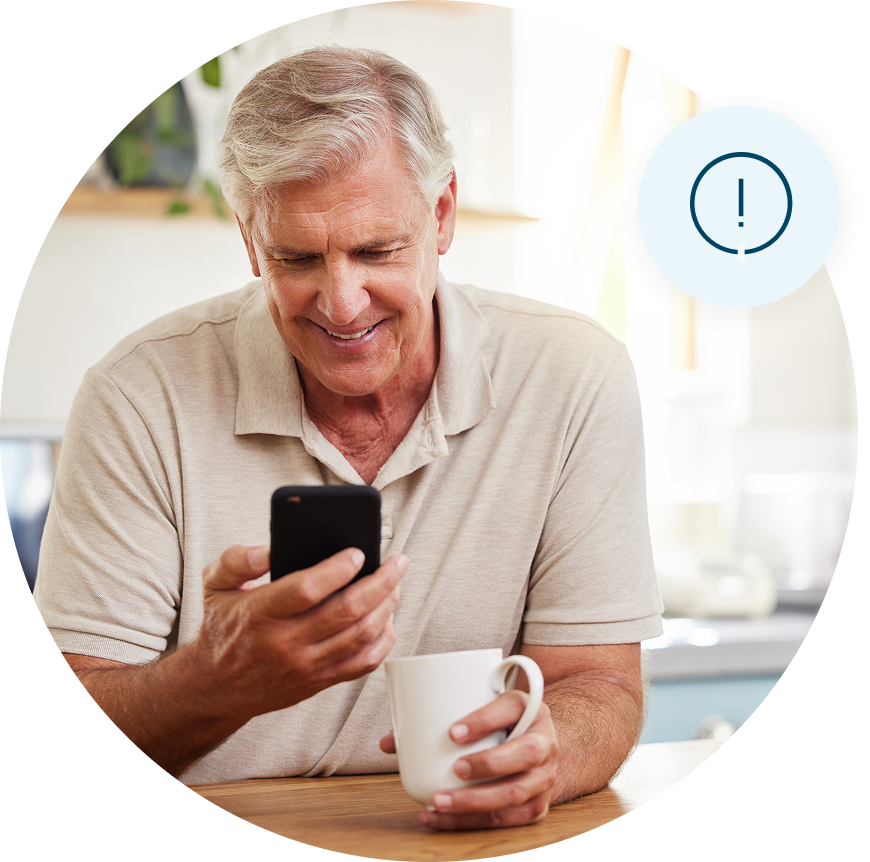 Man sitting a table with coffee in one hand and a cell phone in the other hand