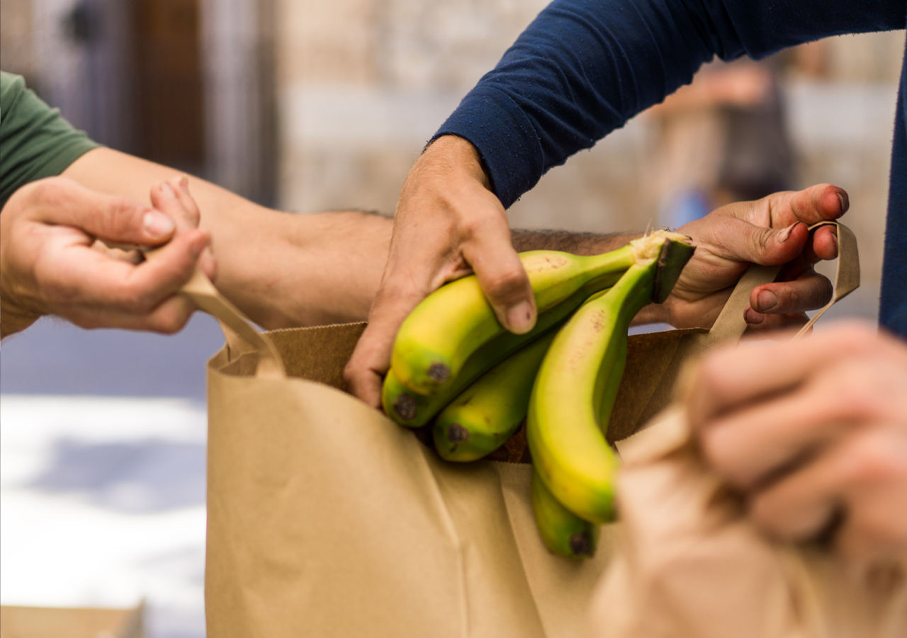 hands putting a bunch of bananas into a paper shopping bag