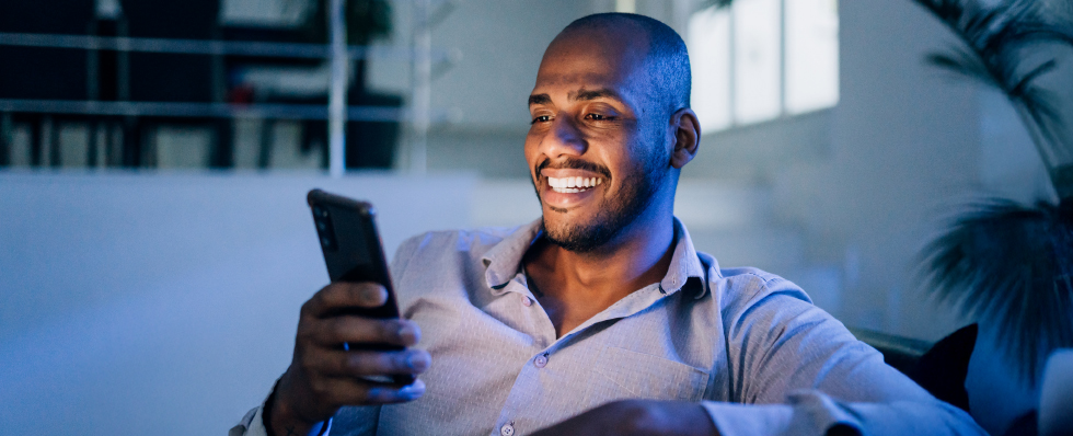 man looking at mobile phone screen illuminating on his smiling face