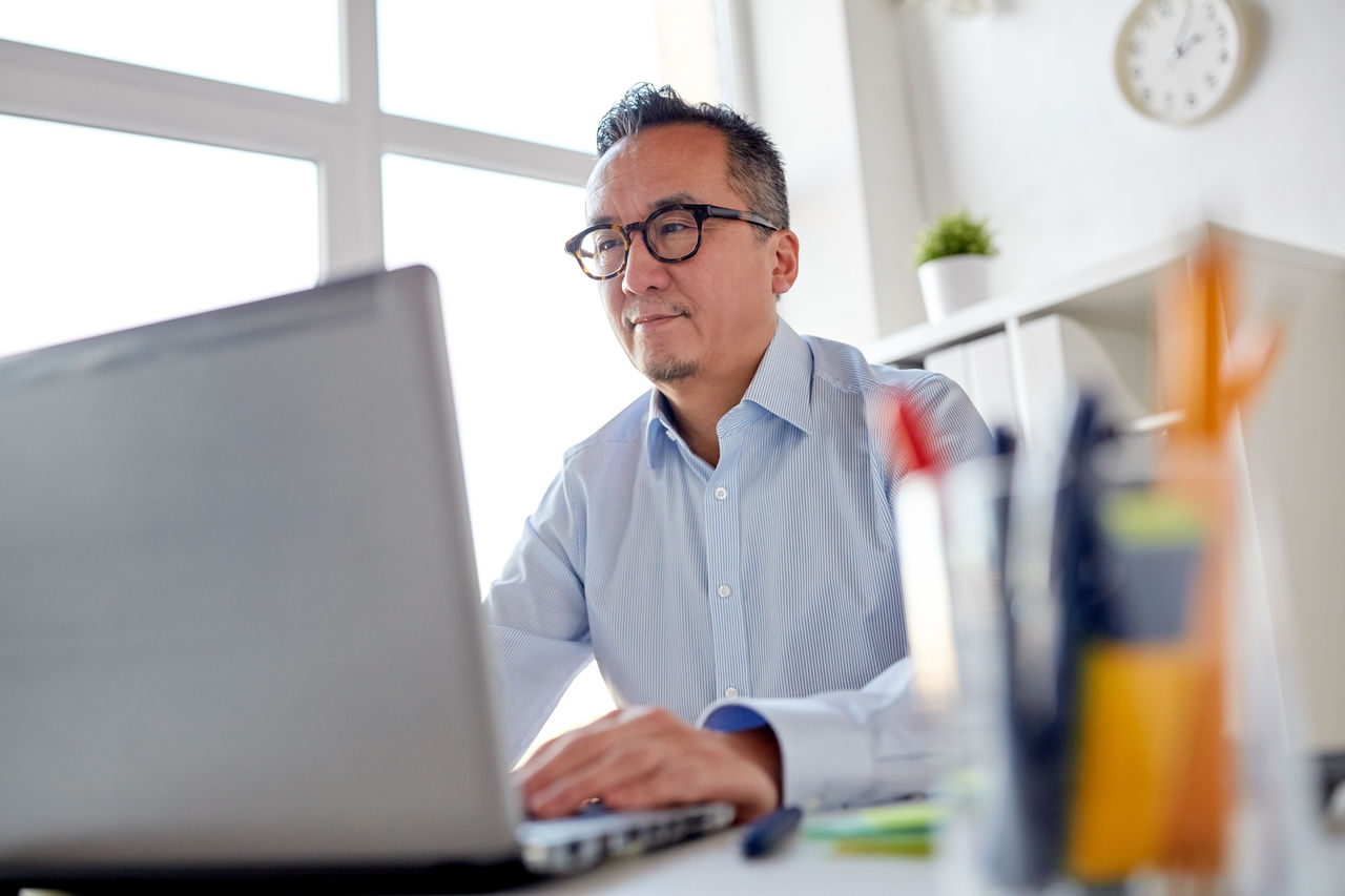 business, people and technology concept - businessman in eyeglasses with laptop computer office